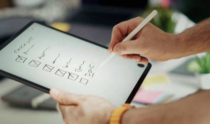 Close-up of a hand writing on a digital checklist using a stylus on a tablet, enhancing productivity.