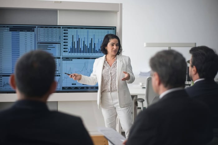 Professional woman presenting stock market data in a modern office setting.