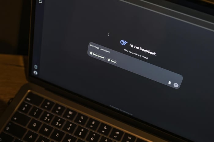 A laptop on a wooden table shows an AI chat interface, featuring the DeepSeek chatbot in action.