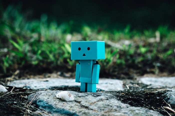 Cute blue toy robot standing on a rocky path surrounded by greenery.